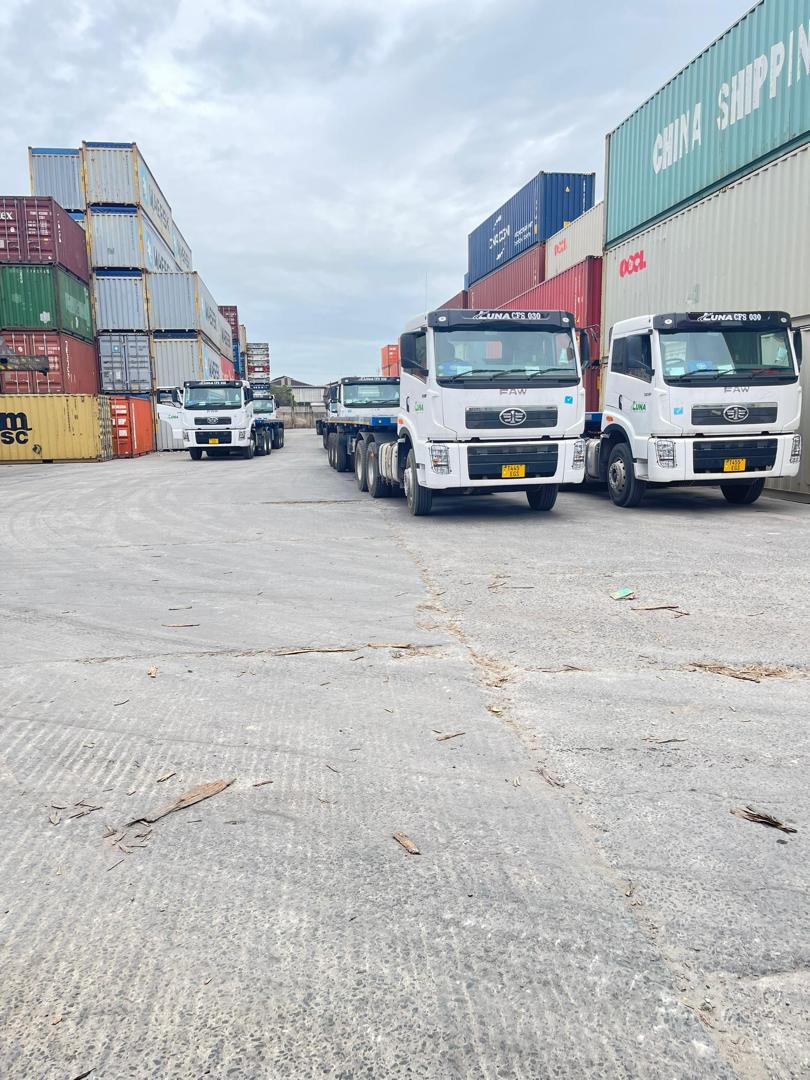 Truck fleet lined up beside stacked containers